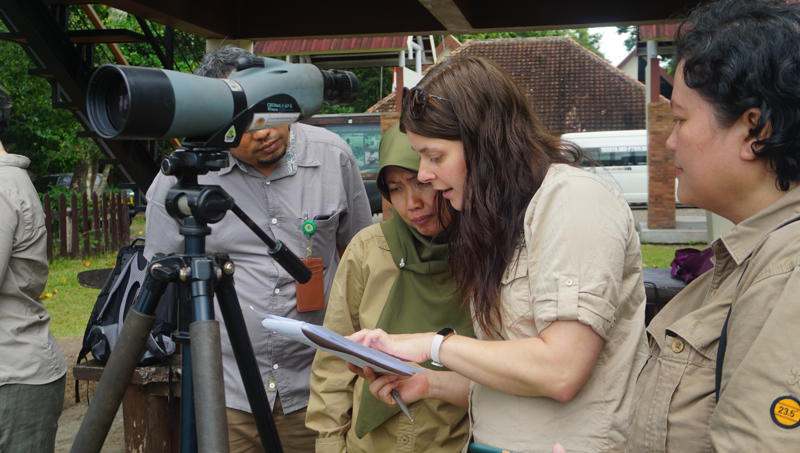 Amy Humphreys, a woman with long dark hair, with a group of field workers. They are standing beside a telescope.