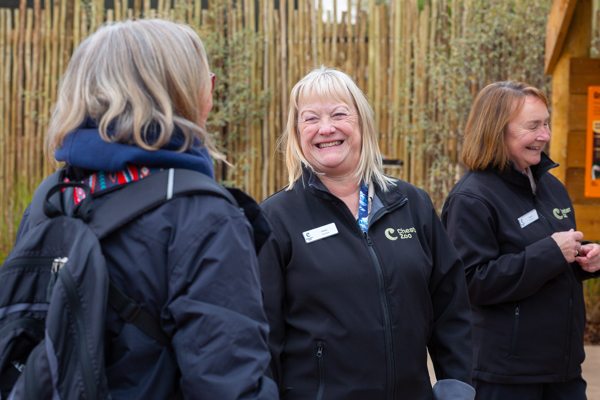 Two smiling volunteers talking to a visitor at Chester Zoo